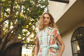 Woman in a floral dress standing outdoors with trees and a building in the background