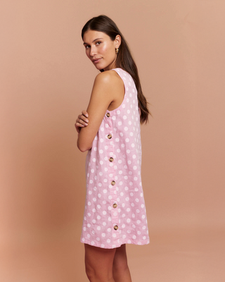 Woman wearing a pink polka dot dress with gold buttons on a beige background